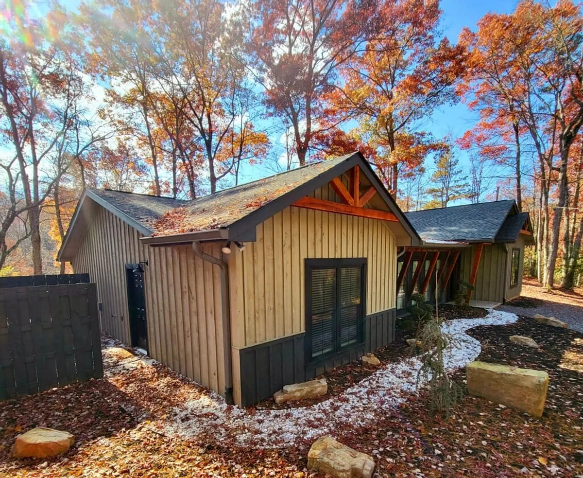 This image presents the wooden exterior of the property nestled among trees, with a sloped roof and a stone-lined pathway leading into the woods. It conveys a sense of tranquility, natural beauty, and outdoor enjoyment.