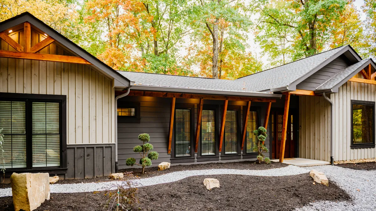 The image showcases the chalet's modern architecture with warm wood accents, surrounded by lush landscaping and towering trees. The inviting outdoor space features a cozy fire pit area, perfect for relaxing in the serenity of the Smoky Mountains.