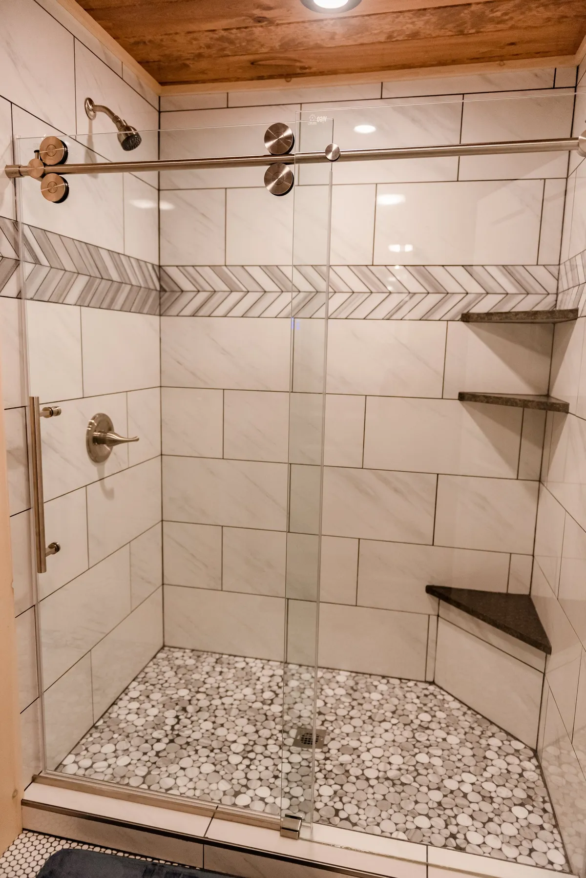 A modern bathroom with a glass-enclosed walk-in shower, textured tile, marble wall accents, and a pebble floor. The ambiance is spa-like and rejuvenating, emphasizing the experience of a relaxing and invigorating shower.