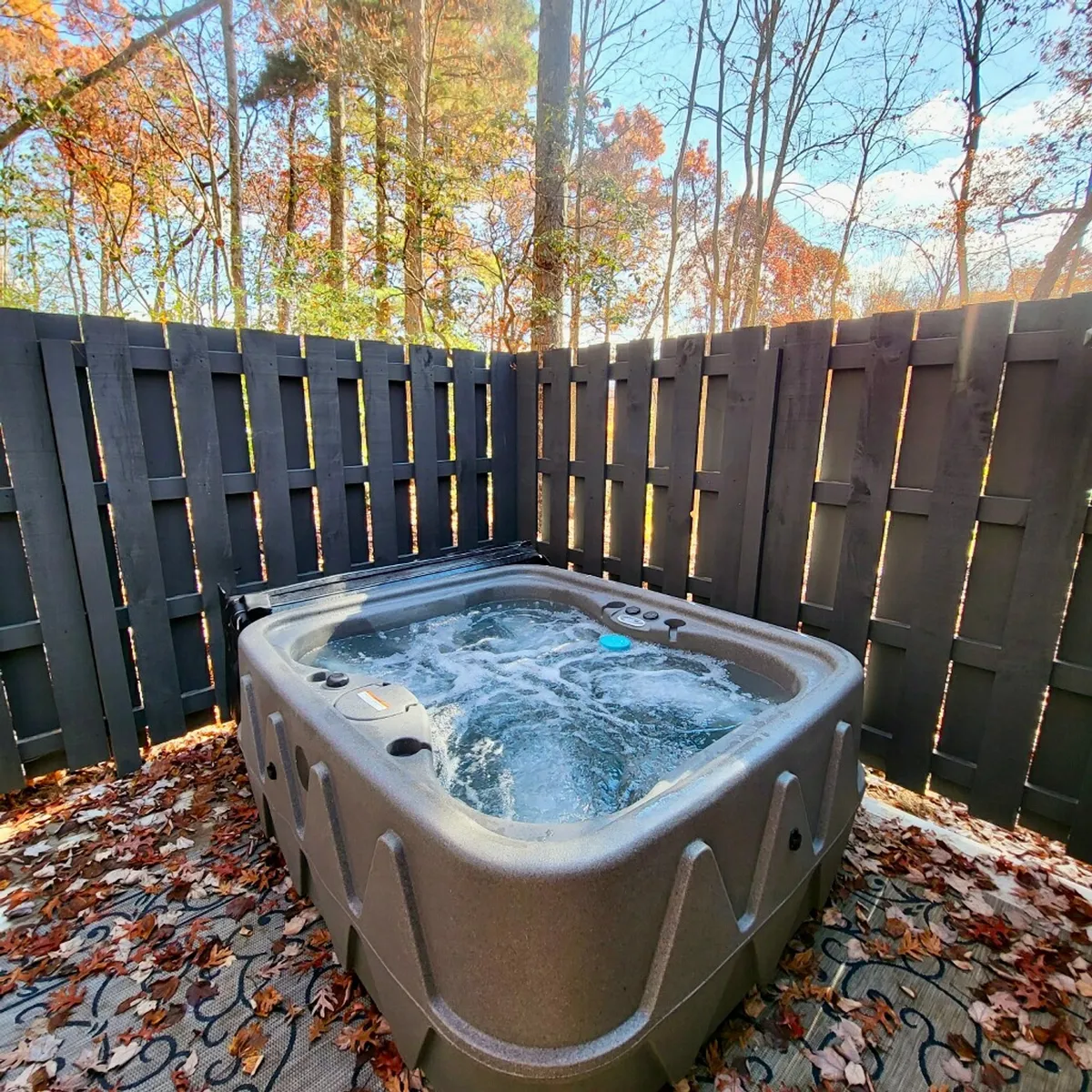 An inviting outdoor hot tub nestled among trees and autumn leaves, with a tranquil, natural setting perfect for unwinding under the stars. The image evokes peace and solitude, echoing the exclusive back porch and hot tub access from the master suite.