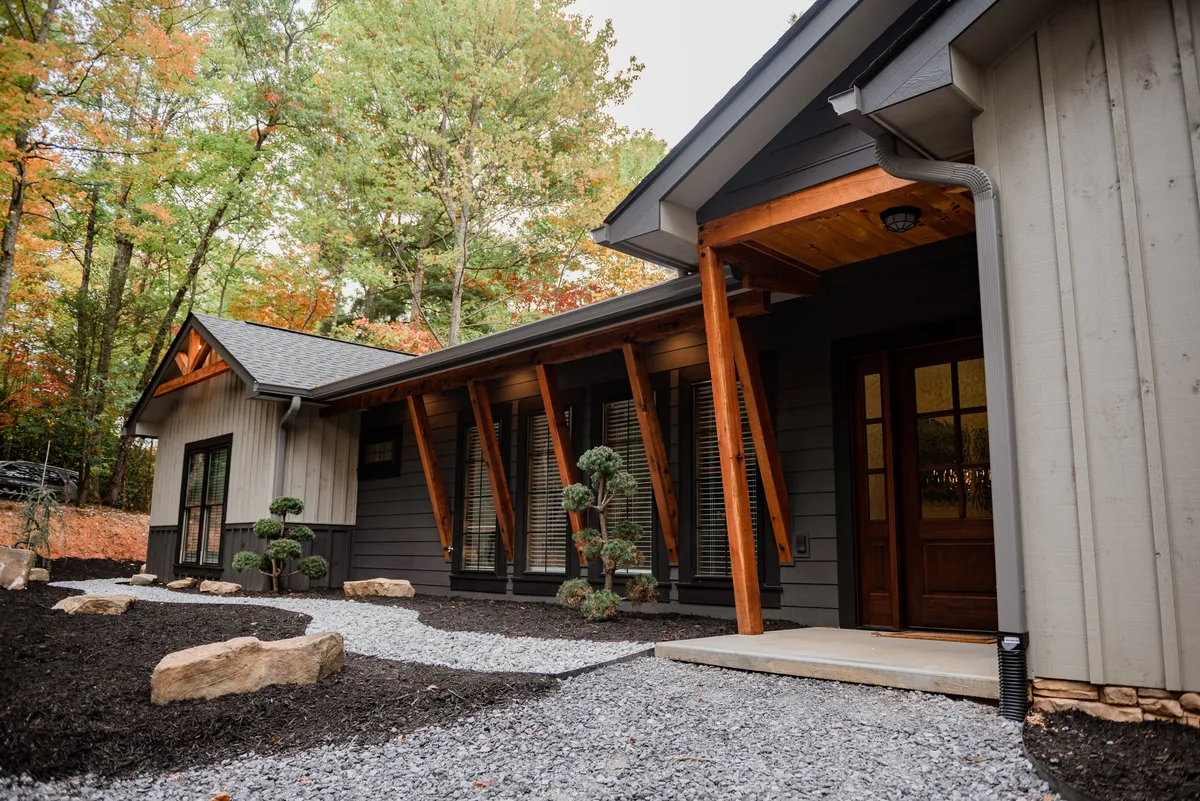 This inviting exterior shot focuses on the welcoming entrance, with decorative shrubs, sturdy wooden beams, and a gravel pathway leading up to the porch—an ideal spot for morning coffee and evening chats.