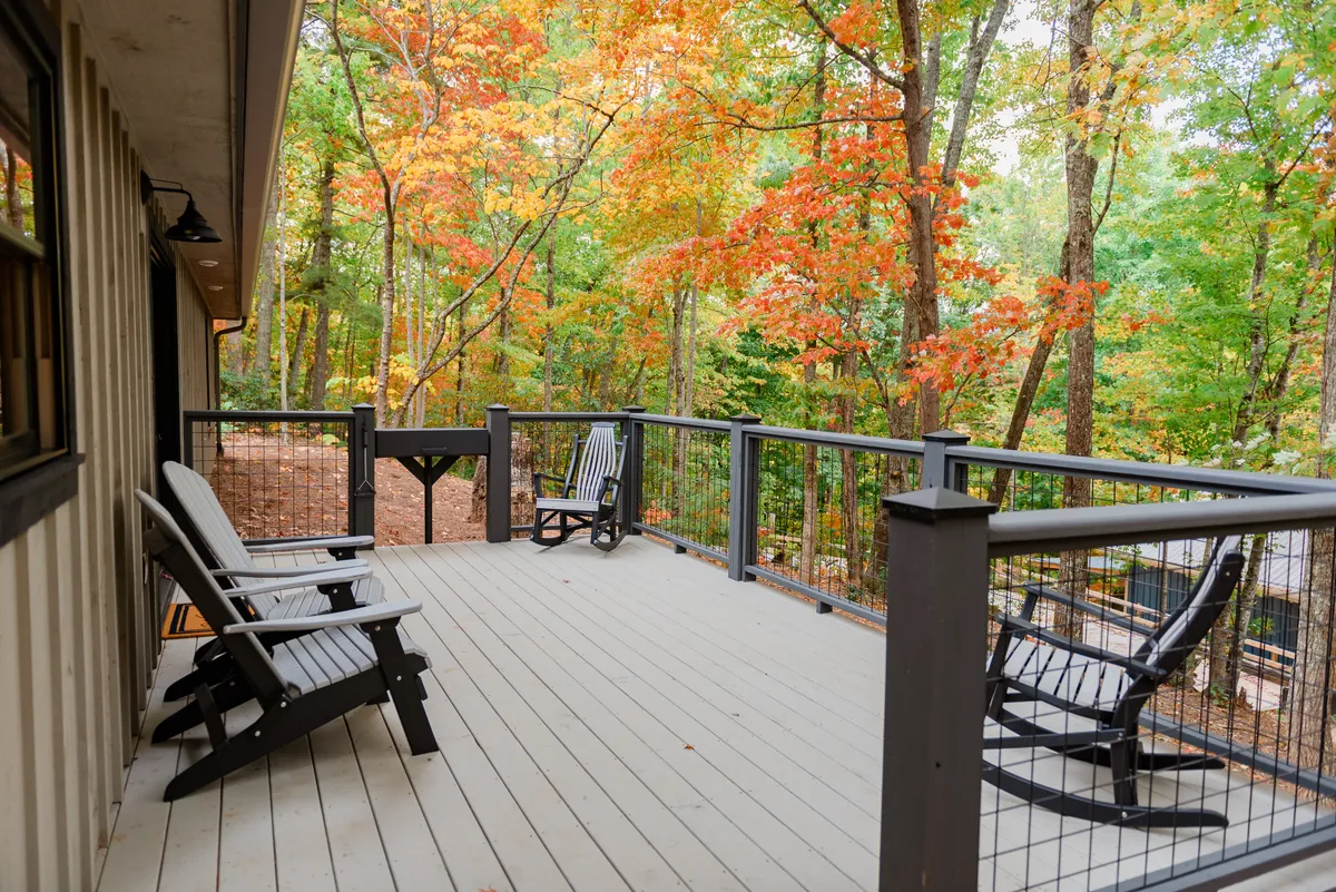 A spacious deck features comfortable chairs and a sturdy railing, all surrounded by vibrant foliage. The space invites guests to relax with a book or a drink in hand, while taking in the sights and sounds of the forest.