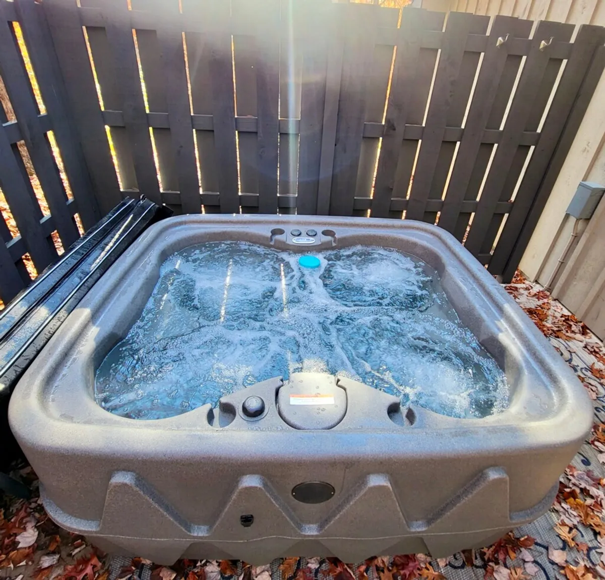 A private outdoor hot tub is nestled on a wooden deck, surrounded by a rustic wooden fence and vibrant autumn leaves. The scene radiates tranquility, with the inviting water promising relaxation and the natural setting reinforcing the secluded woodland feel.